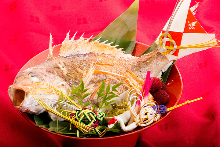 祝い飾りと笹の葉を添えて盛り付けた鯛の塩焼きのお頭付き料理を器に盛ったお祝い膳の写真