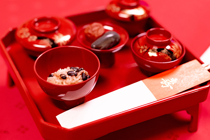 朱塗りの御膳に赤飯や煮物、吸い物を揃えたお食い初め祝いの料理セットの盛り付け写真