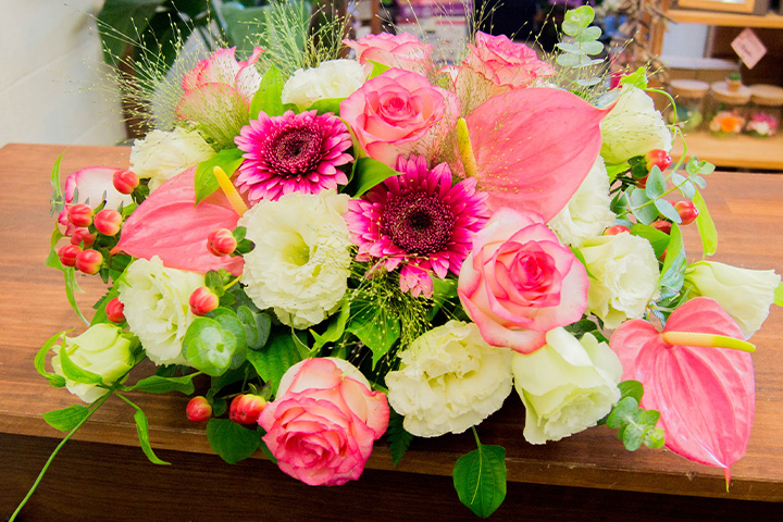 ピンクのバラやガーベラ、アンスリウムを使った華やかなテーブル装花のフラワーアレンジメントの写真