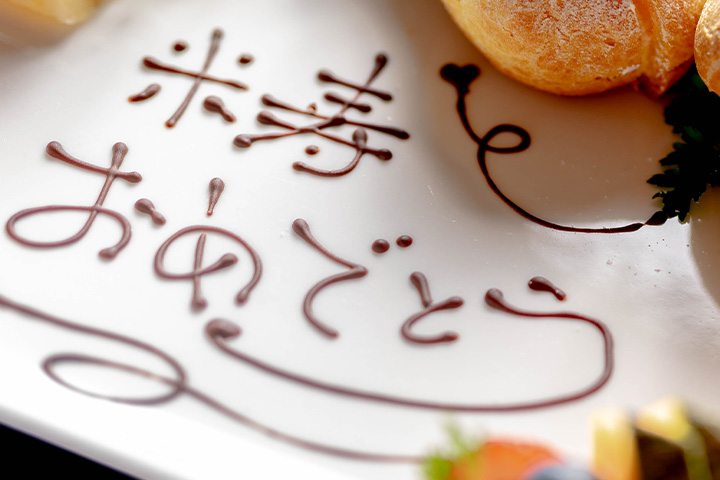 デザートプレートにチョコレートで「卒寿おめでとう」と描かれたお祝いメッセージの演出写真