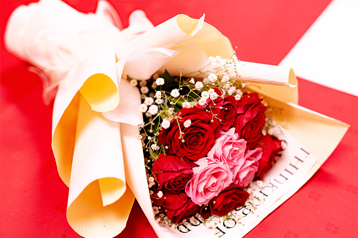 赤とピンクのバラを束ねた華やかな花束を祝いの席のテーブルに置いたギフト用ブーケの写真