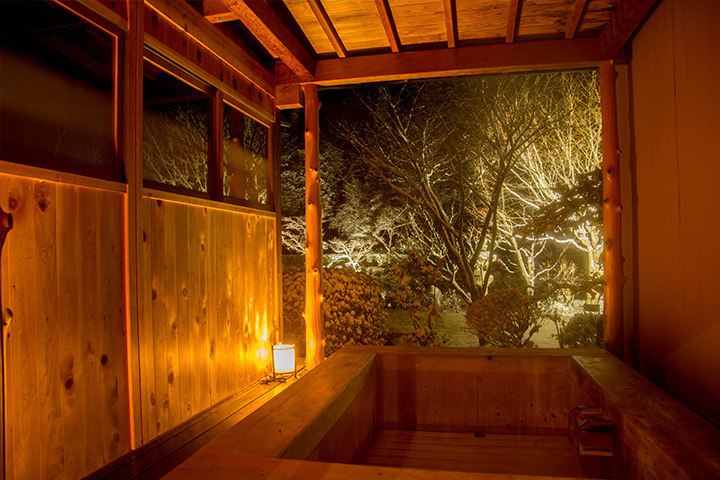 夜の雪景色を望む、料亭ゆう月の木造露天風呂。やわらかな照明に包まれた静かな湯の空間