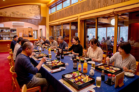 庭園を望む店内で団体旅行のお食事を楽しむお客様。京都府綾部市の料亭ゆう月は最大50名様まで対応しております。