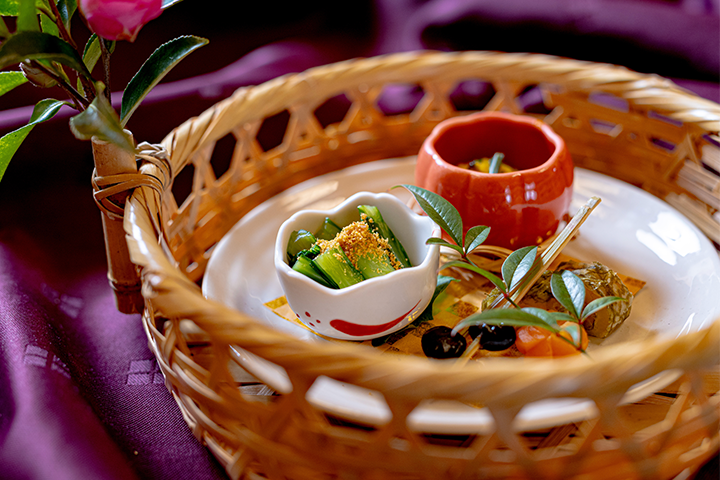 冬の会席前菜の盛り合わせ。真鯛の白板昆布巻き、牡蠣と菊菜の黄身酢和え、菜の花の唐墨和え、黒豆松葉串を籠盛りにした料理写真。