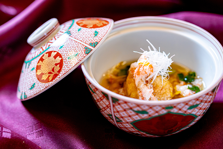 蒸し器でふっくらと仕上げた海老芋まんじゅうに蟹あんをかけ、白髪ねぎを添えた冬の蒸し物料理。朱色と金彩の蓋付き器に盛り付けられた上品な一品