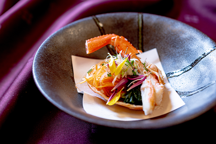 カニの土佐酢漬けを甲羅に盛り付けた酢の物。むき身のカニ脚、人参の土佐酢漬け、菜の花、薬味を彩りよく添えた冬の一皿。