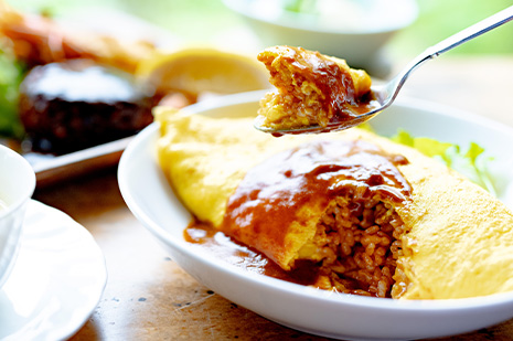 デミグラスソースをかけたオムライスをスプーンですくう瞬間。中のケチャップライスが見える温かい洋食ランチセット