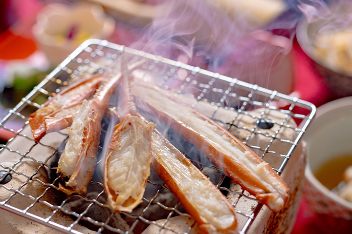 炭火で焼かれる松葉ガニの脚,香ばしい湯気が立ちのぼる冬の会席料理の一品